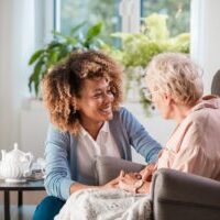 Female home caregiver talking with senior woman, sitting in living room and listening to her carefully.